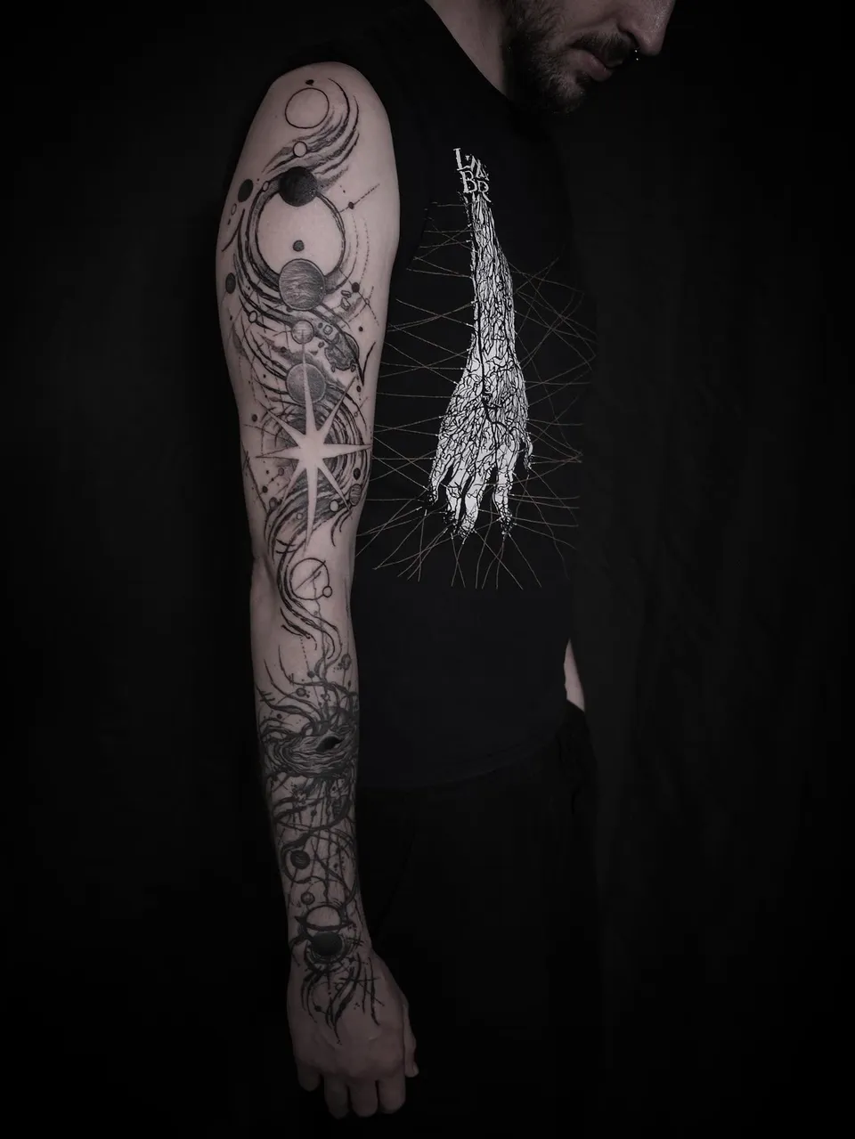 Blackwork sleeve of planets, a star and roots down the arm