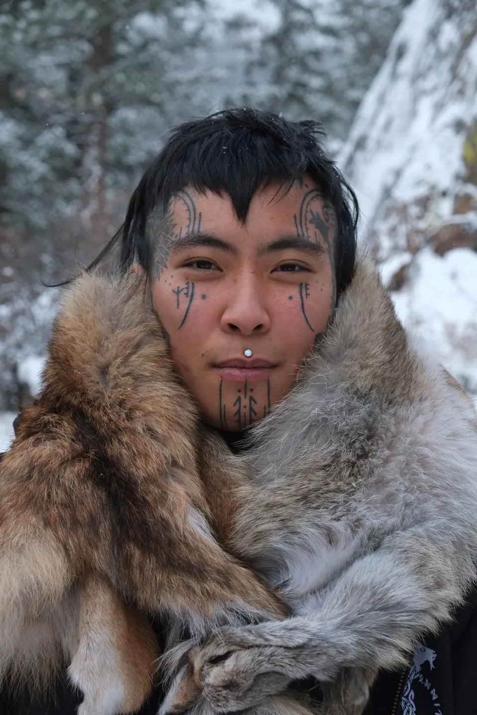 Ornamental face tattoos on a person wrapped in fur, in the snow